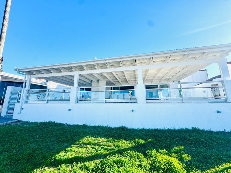 A well-maintained covered patio featuring a modern glass balustrade, exposed white timber rafters, and a clean, bright exterior finish overlooking the garden.