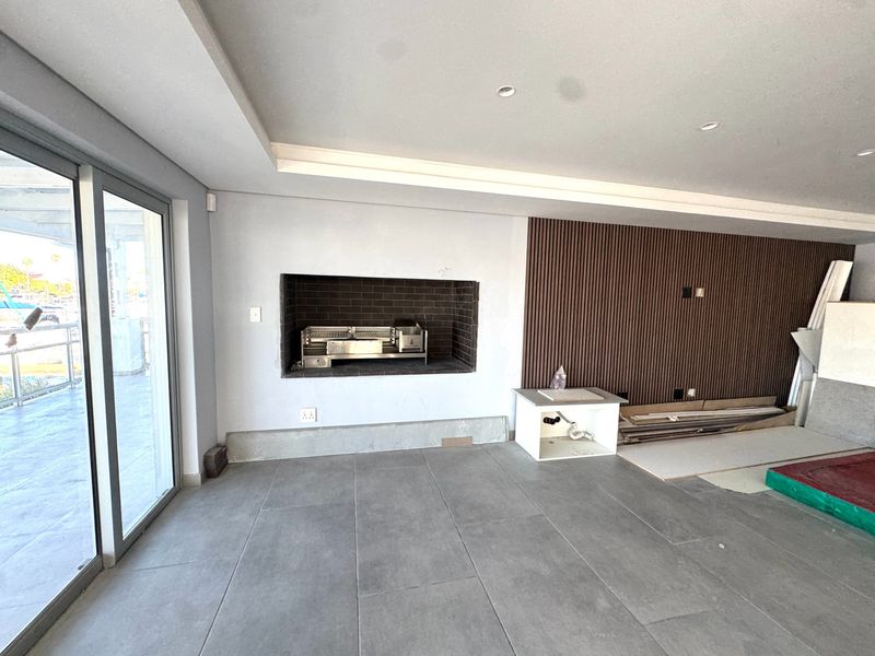 An unfinished patio area featuring a built-in braai, modern tiled flooring, and decorative timber slat wall paneling, awaiting final completion and installation.