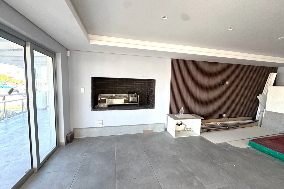 An unfinished patio area featuring a built-in braai, modern tiled flooring, and decorative timber slat wall paneling, awaiting final completion and installation.