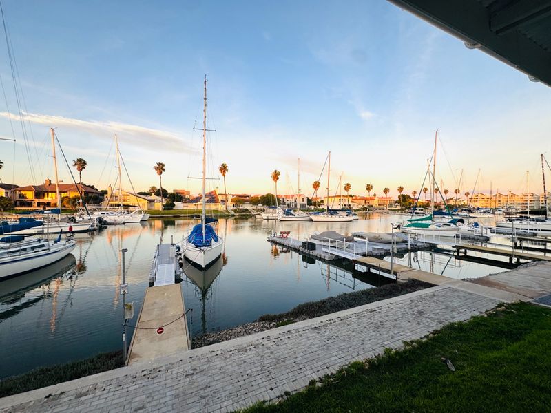 A scenic view of a private marina featuring multiple sailboats moored at jetties, captured at sunset from a paved waterfront area.