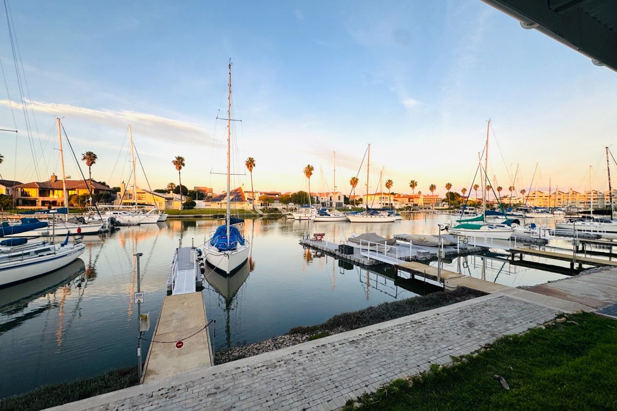 A scenic view of a private marina featuring multiple sailboats moored at jetties, captured at sunset from a paved waterfront area.