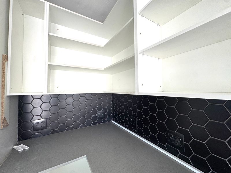 A modern scullery or prep area featuring clean white built-in cabinetry, a dark stone countertop, and a stylish black hexagonal tile backsplash.