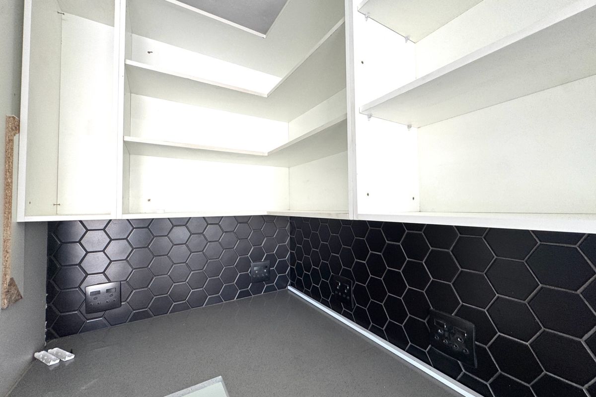 A modern scullery or prep area featuring clean white built-in cabinetry, a dark stone countertop, and a stylish black hexagonal tile backsplash.