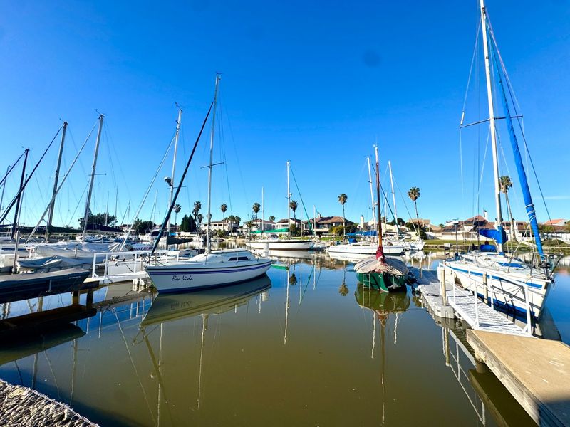 A scenic view of a tranquil marina featuring multiple sailboats moored at floating jetties under a clear blue sky.