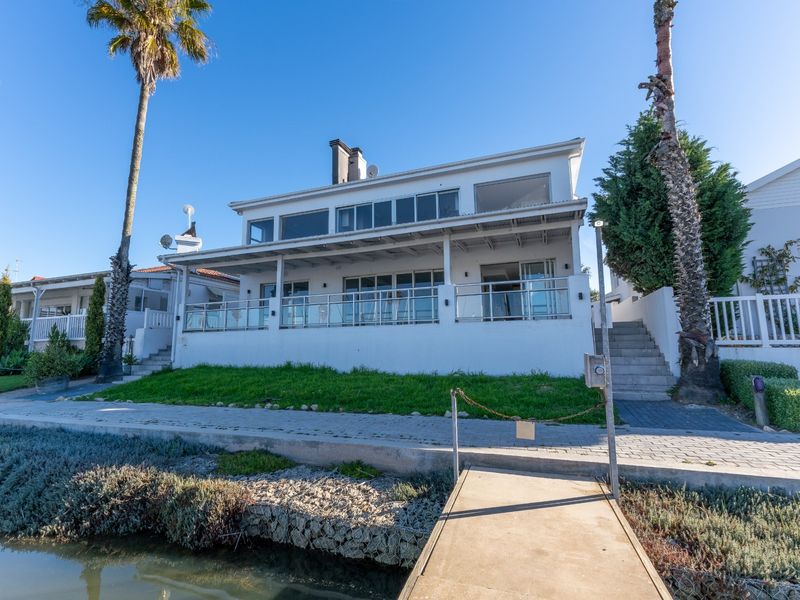 Rear view of a waterfront property featuring a covered patio, glass balustrades, and a private jetty leading to the water.