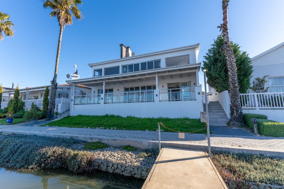 Rear view of a waterfront property featuring a covered patio, glass balustrades, and a private jetty leading to the water.
