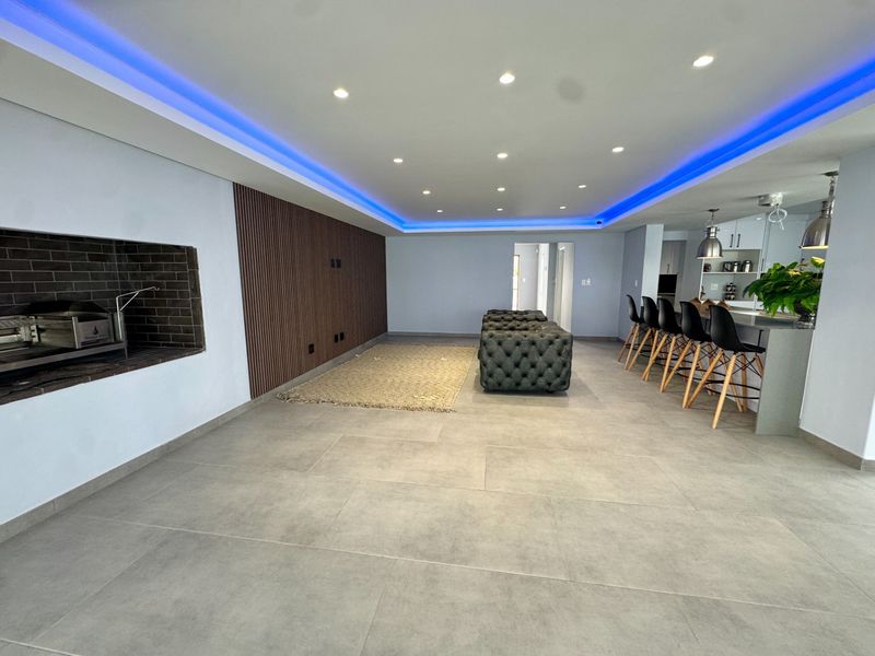 Spacious open-plan living area featuring modern porcelain tiling, recessed LED lighting, a built-in braai, and a contemporary kitchen island with bar seating.
