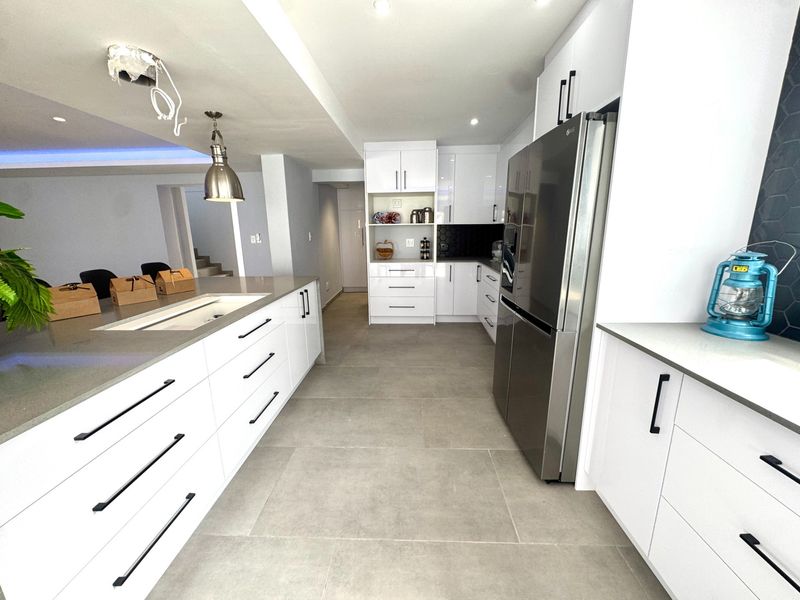 Modern kitchen featuring white high-gloss cabinetry, quartz countertops, a central island, and stylish hexagonal backsplash tiles with contemporary recessed and pendant lighting.