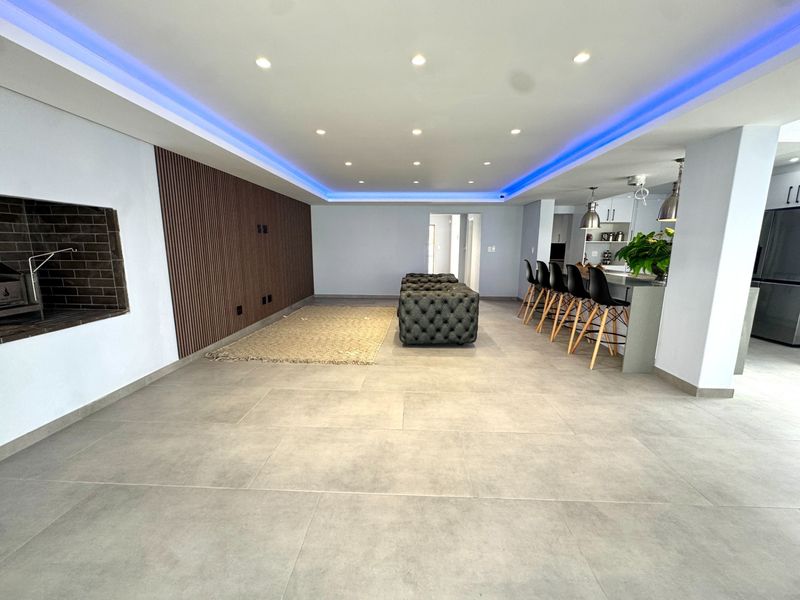 Spacious open-plan living area featuring large format floor tiles, a built-in fireplace, decorative slatted wood wall paneling, and a modern kitchen island with bar seating.