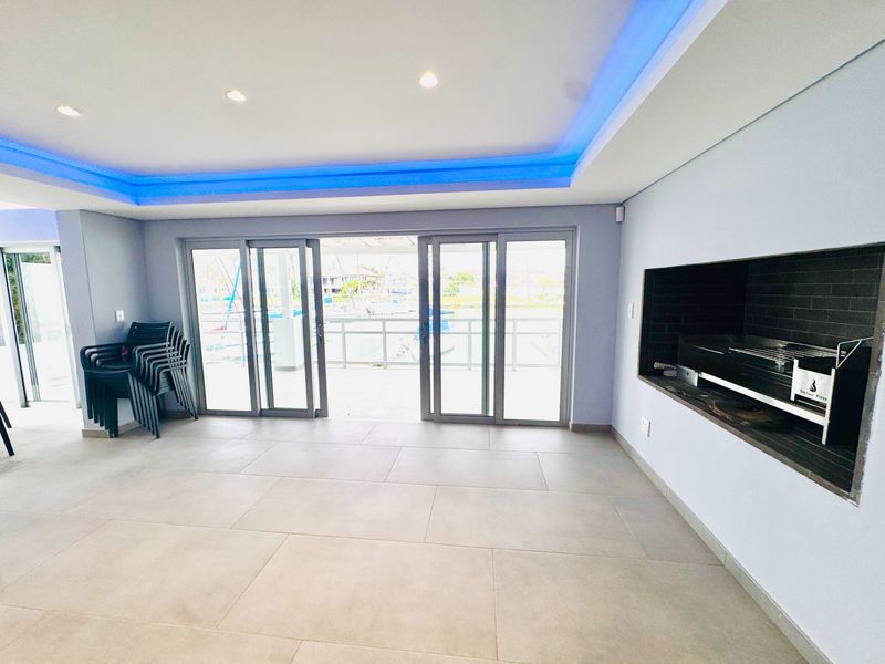 Spacious living area featuring a built-in braai, modern recessed and cove lighting, and large sliding doors opening to an outdoor view.