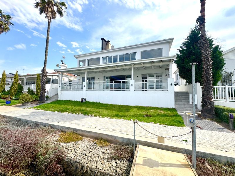 Rear view of a two-story house featuring a covered patio, glass balustrades, and a well-maintained lawn area.