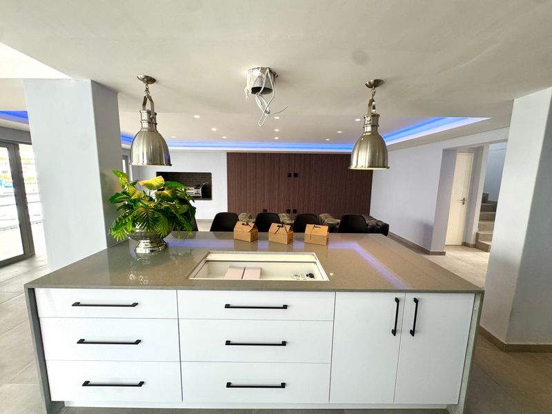 Modern open-plan living area featuring a central kitchen island with stone countertops, sleek cabinetry, and contemporary slatted wood wall accents with ambient lighting.