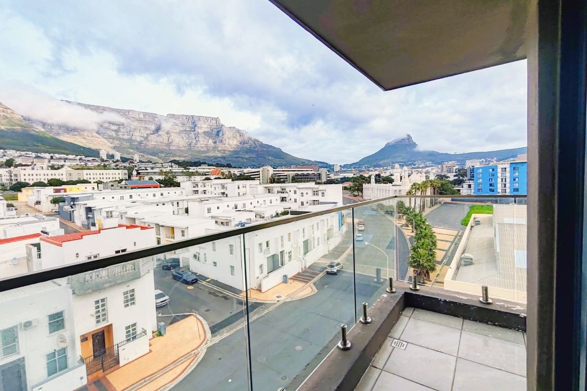 A spacious balcony featuring a modern glass balustrade and tiled flooring, offering expansive views of the surrounding cityscape and mountain range.