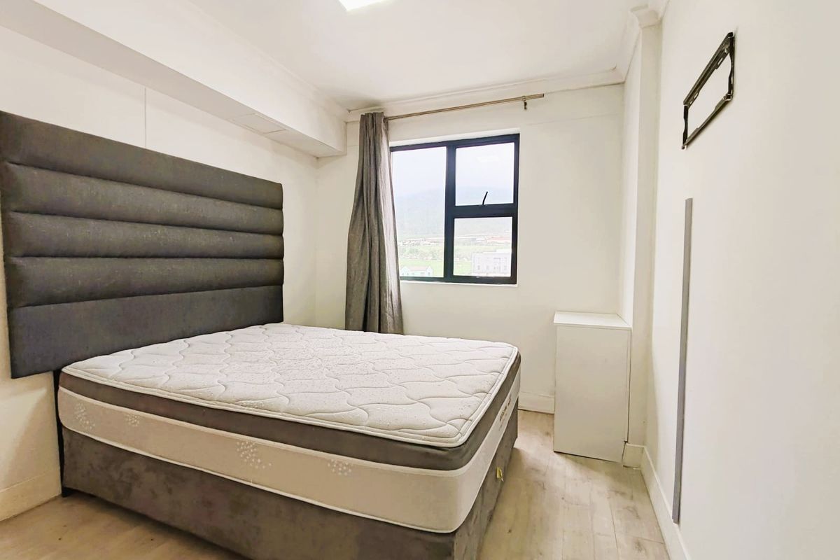A bedroom featuring laminate flooring, neutral walls, and an aluminium-framed window with views.