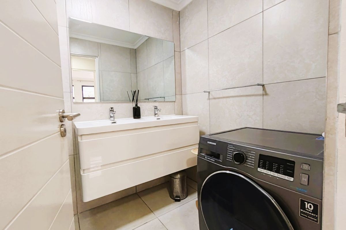Modern bathroom featuring a sleek double vanity with integrated sinks, large wall-mounted mirror, and neutral floor-to-ceiling tiling.