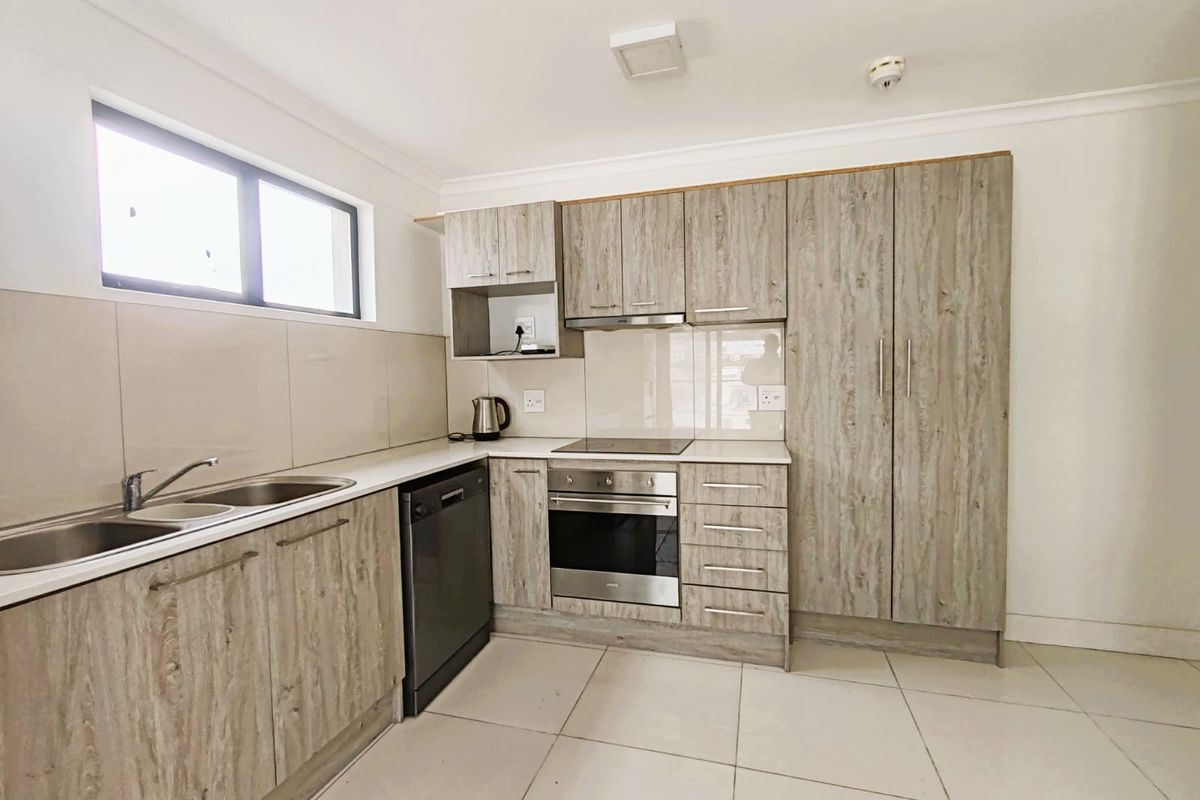 Modern kitchen featuring light wood-grain cabinetry, integrated appliances, stainless steel sink, and neutral tiled flooring with a clean, contemporary finish.
