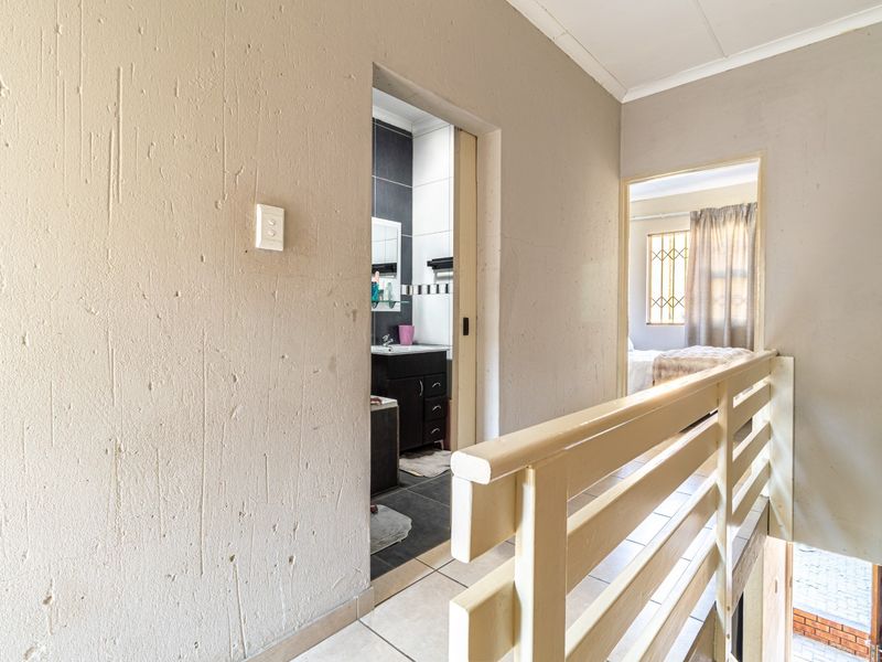 A hallway featuring a timber balustrade, tiled flooring, and access to an adjacent bathroom and bedroom.