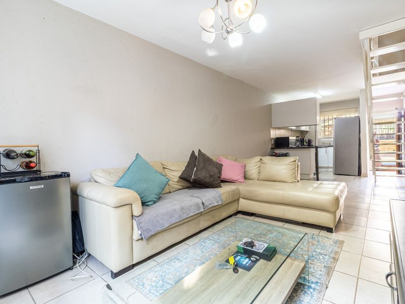 Open plan living area featuring tiled flooring, a staircase, and a functional kitchen space in the background.