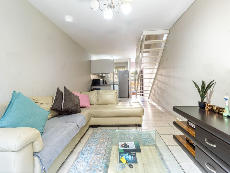 Open plan living area featuring tiled flooring and a staircase, leading through to a functional kitchen space.