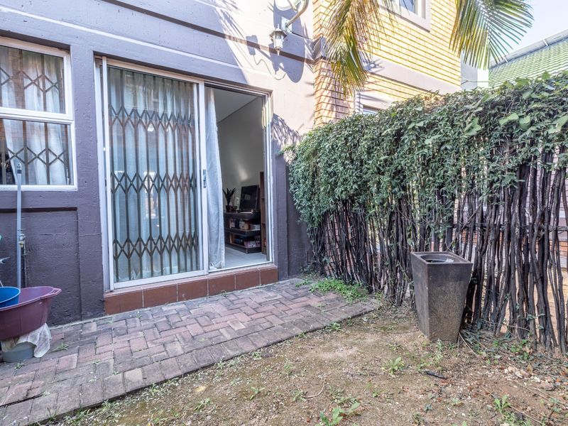 Rear exterior view featuring a paved patio area, sliding glass door with security gate, and established garden screening.