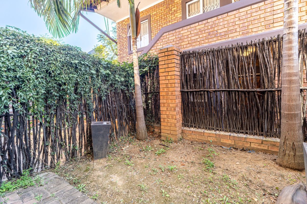A rear exterior view showing a brick wall, timber stick fencing, and a small patch of garden with paved access.