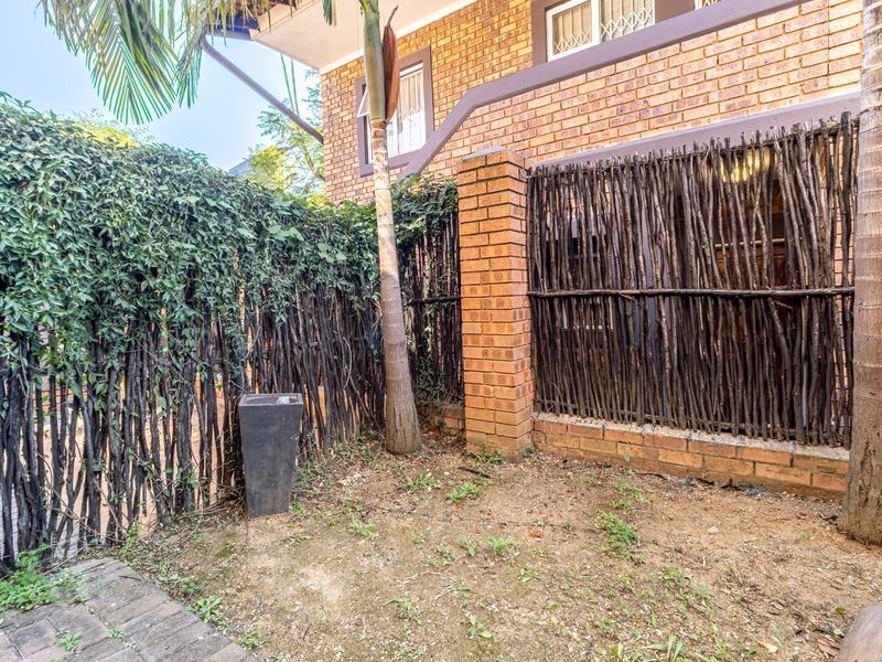 A rear exterior view showing a brick wall, timber stick fencing, and a small patch of garden with paved access.