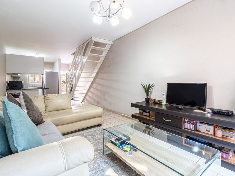 Open-plan living area featuring tiled flooring, a central staircase, and an integrated kitchen space with functional cabinetry.