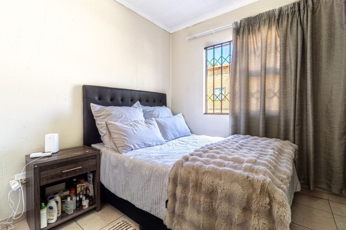 A compact bedroom featuring tiled flooring, a window with security bars, and neutral wall finishes.