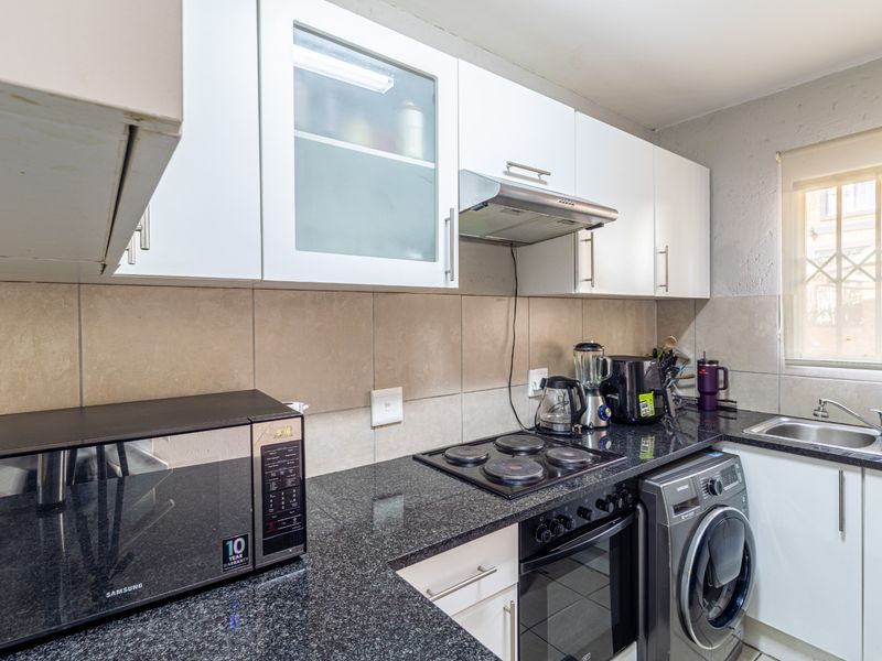 A functional kitchen featuring granite countertops, a tiled backsplash, built-in oven with electric hob, extractor fan, and ample upper and lower cabinetry.
