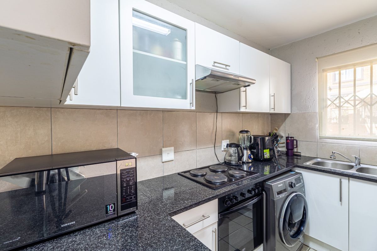 A functional kitchen featuring granite countertops, a tiled backsplash, built-in oven with electric hob, extractor fan, and ample upper and lower cabinetry.