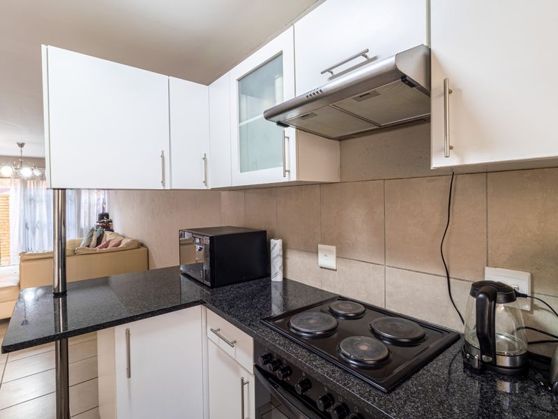 A functional kitchen featuring granite countertops, built-in electric hob, oven, and stainless steel extractor fan, with ample upper and lower cabinetry.