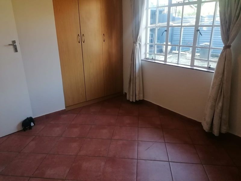 A vacant bedroom featuring built-in wooden cupboards, terracotta-style tiled flooring, and a window with security bars.