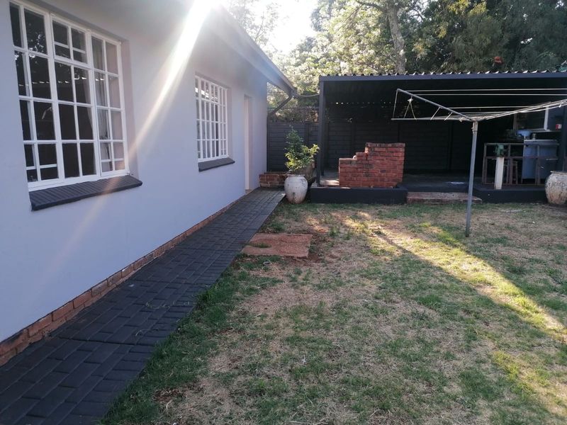 Rear exterior view featuring a paved walkway, covered patio area with a built-in brick braai, and a garden space.