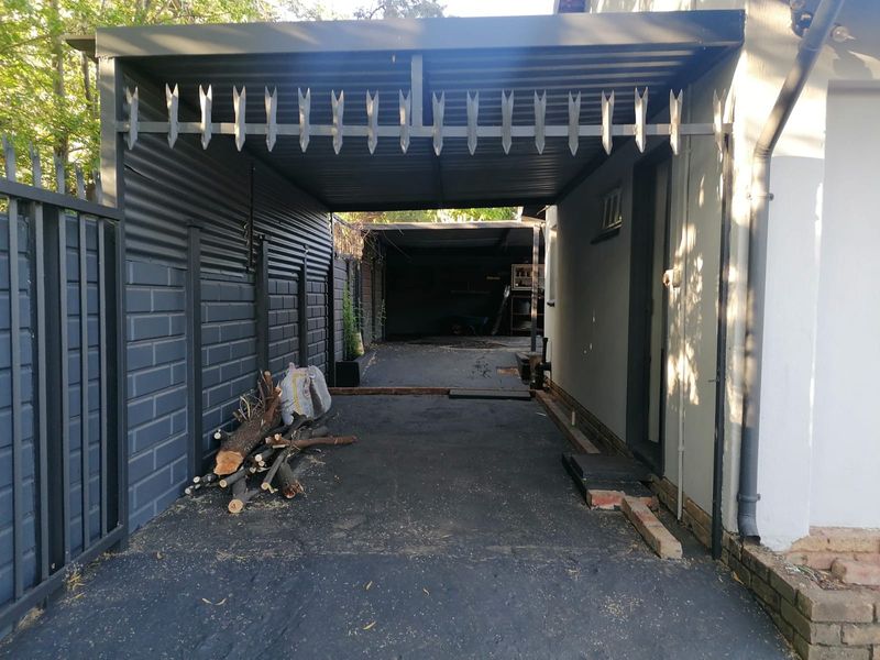 A covered carport area featuring a metal roof, security spikes, and an asphalt driveway, providing sheltered off-street parking.