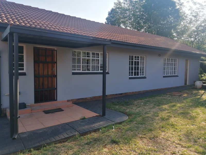 Rear exterior view of the house featuring a covered patio, tiled roof, and paved walkway along the side of the building.