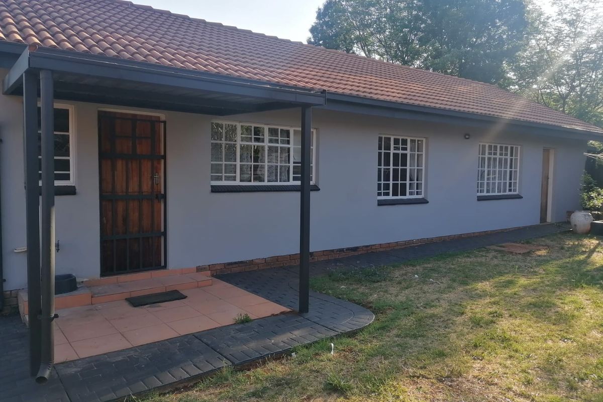 Rear exterior view of the house featuring a covered patio, tiled roof, and paved walkway along the side of the building.
