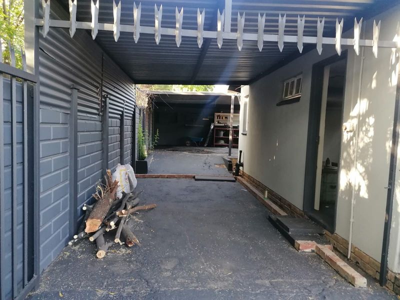 A covered driveway or carport area featuring a corrugated metal roof, paved surface, and secure perimeter walling with spiked security fencing.