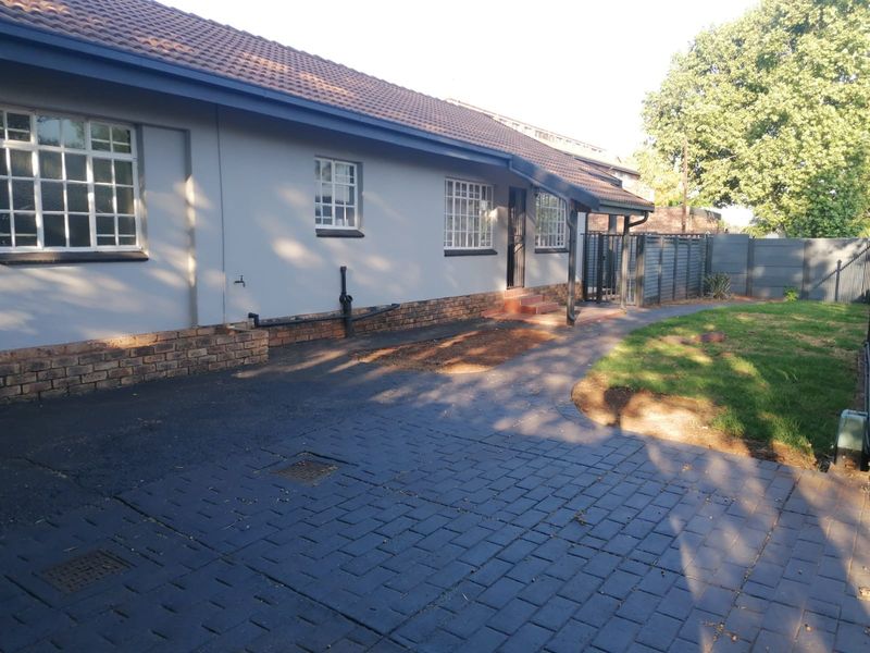 Rear exterior view of the house featuring a tiled roof, paved driveway area, and a small garden space with boundary fencing.
