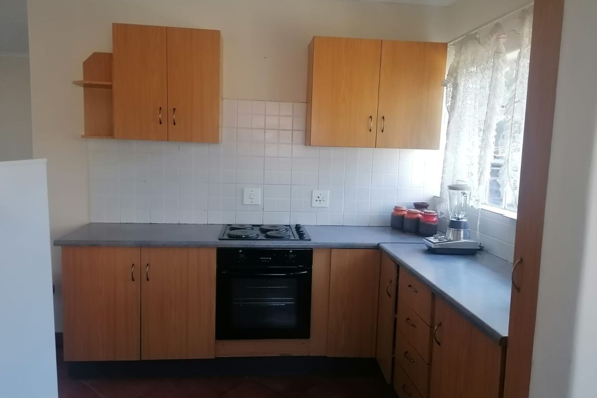 A functional kitchen featuring laminate cabinetry, built-in oven, electric hob, and tiled splashback, offering a practical layout for daily meal preparation.