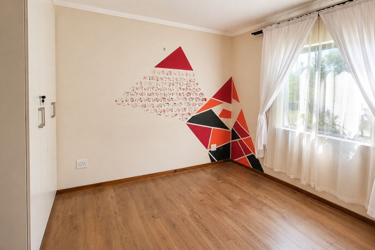 A bright, empty bedroom featuring laminate flooring, a built-in wardrobe, and a window with curtain tracks.