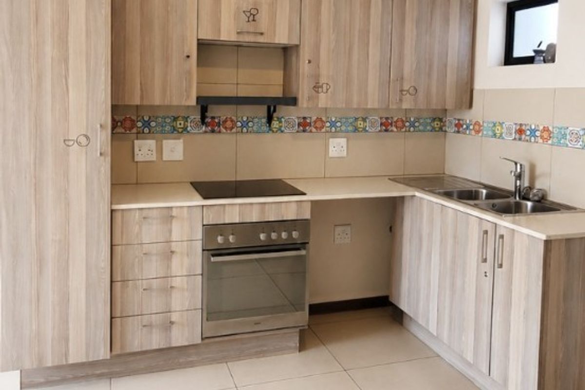 A clean, modern kitchen featuring light wood-grain cabinetry, integrated appliances, a decorative tile backsplash, and neutral floor tiles.
