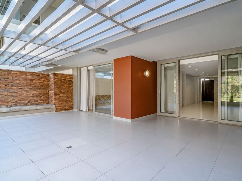 A spacious, modern covered patio featuring a pergola, brick accent wall, built-in bench, and large sliding glass doors leading into the apartment interior.