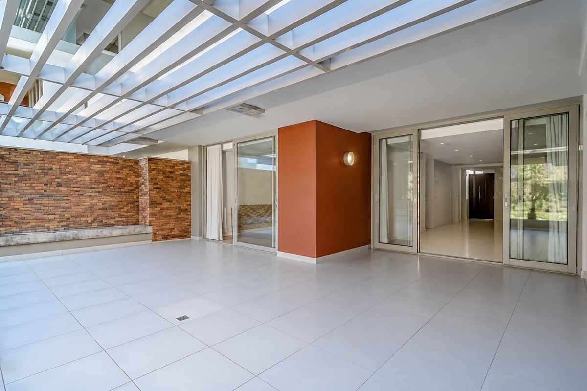 A spacious, modern covered patio featuring a pergola, brick accent wall, built-in bench, and large sliding glass doors leading into the apartment interior.