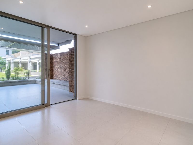 A bright, empty living room featuring large sliding glass doors that open onto a private patio area with modern tiled flooring and recessed lighting.