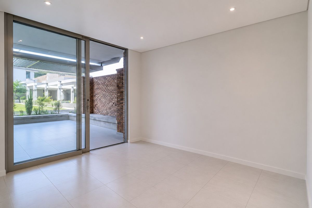 A bright, empty living room featuring large sliding glass doors that open onto a private patio area with modern tiled flooring and recessed lighting.