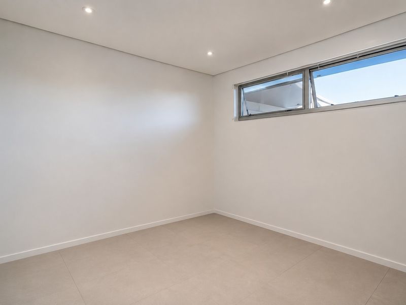 A clean, modern, and empty bedroom featuring neutral tiled flooring, recessed ceiling lighting, and a high-set horizontal aluminium window.