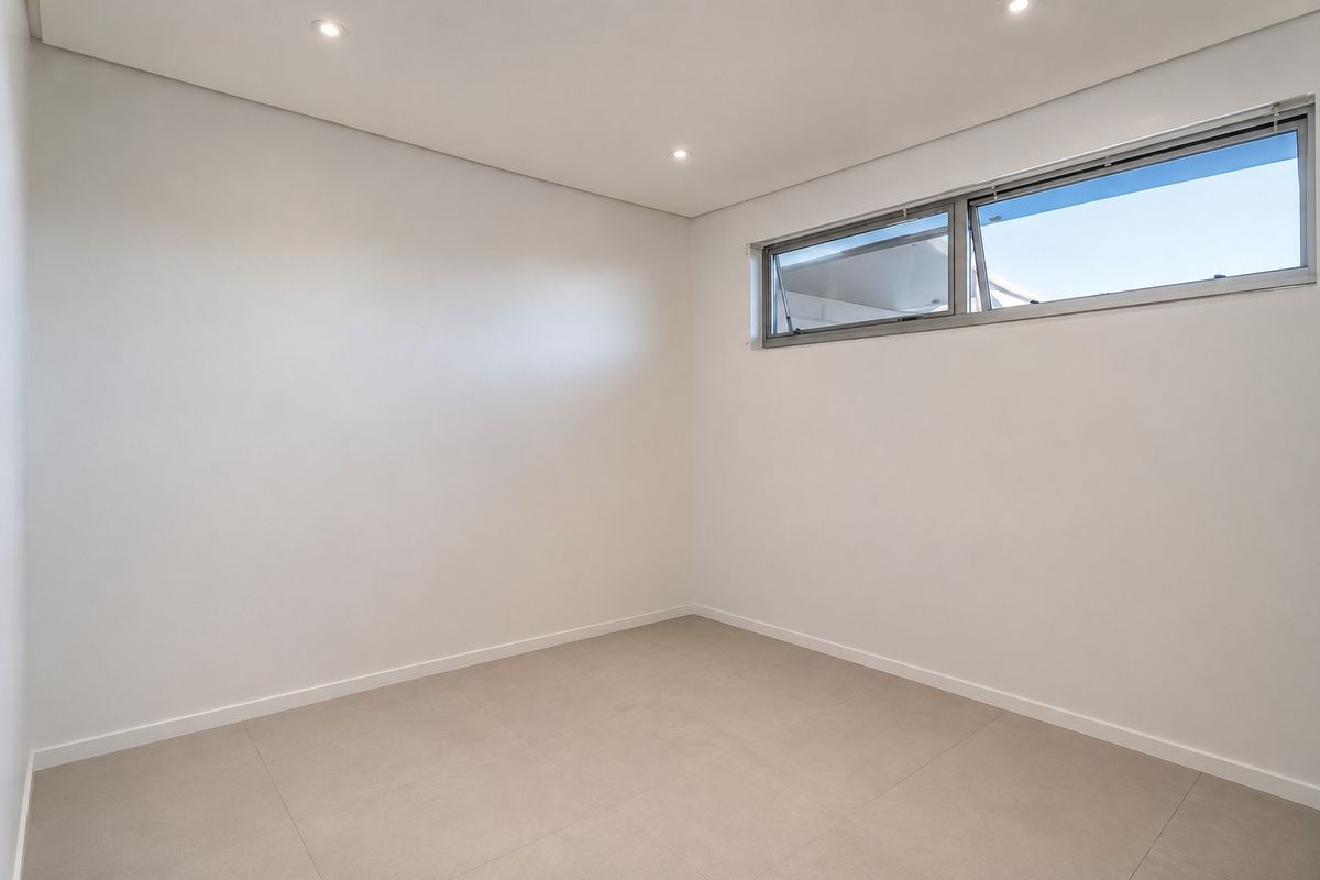 A clean, modern, and empty bedroom featuring neutral tiled flooring, recessed ceiling lighting, and a high-set horizontal aluminium window.