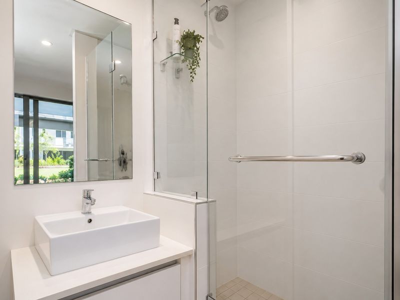 Modern bathroom featuring a clean white vanity basin, wall-mounted mirror, and a spacious walk-in shower with a glass screen and chrome fixtures.