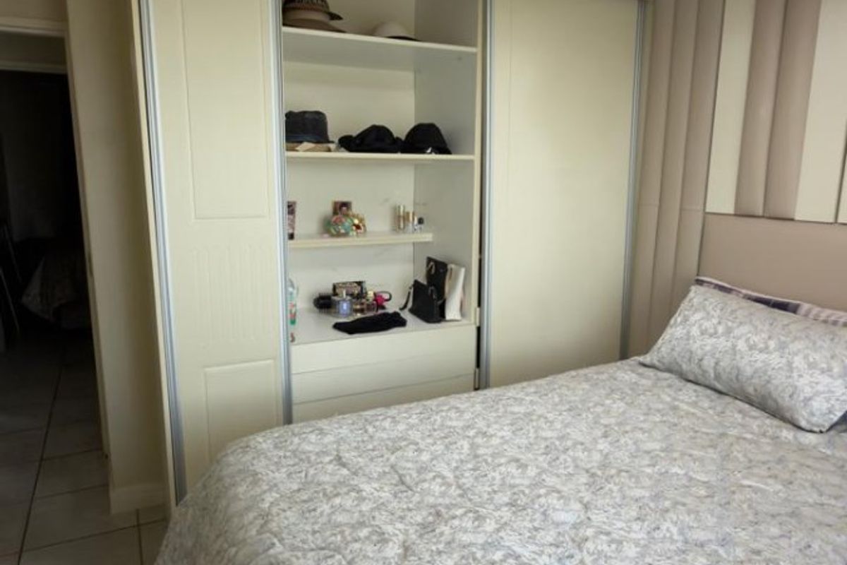 A well-maintained bedroom featuring a built-in wardrobe with sliding doors, a modern ceiling fan, and neutral tiled flooring.