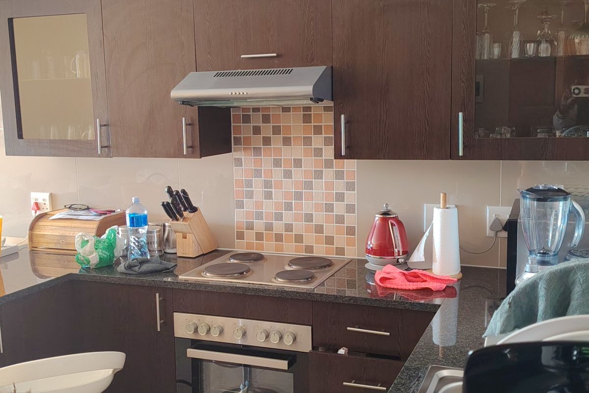 A functional kitchen featuring dark wood cabinetry, granite countertops, a built-in oven with electric hob, and a decorative mosaic tile splashback.